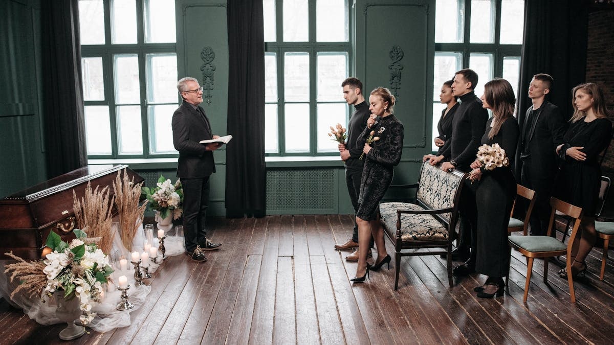 A somber indoor funeral service with people gathered around a coffin, expressing sorrow.