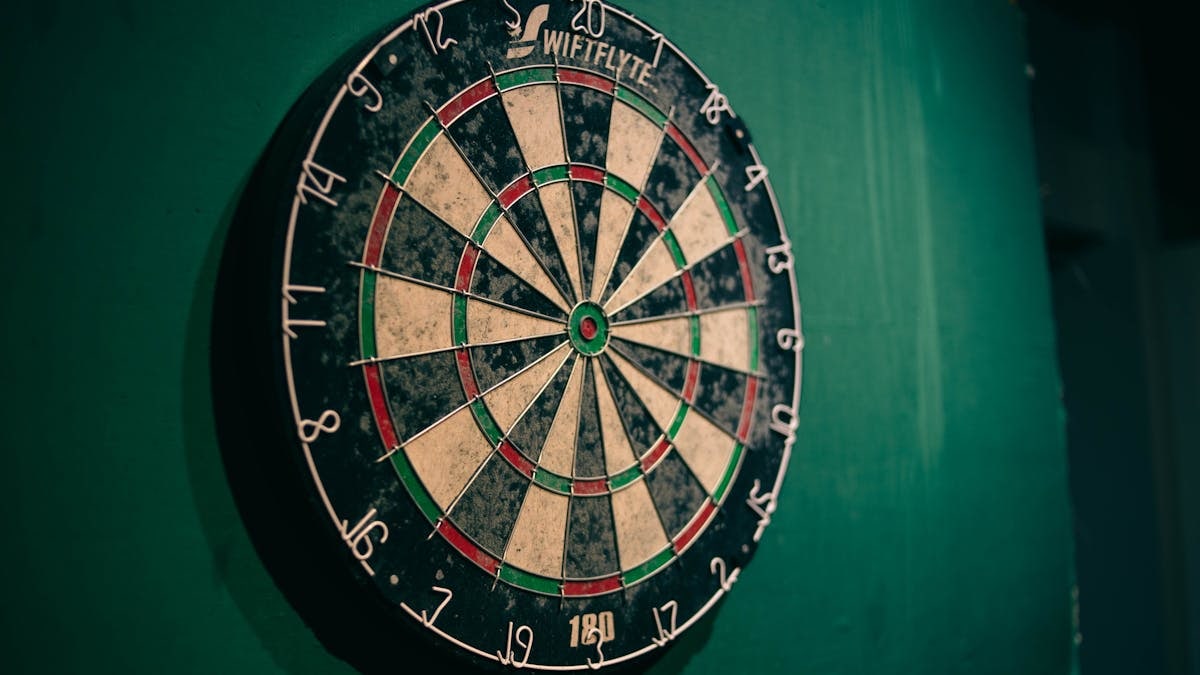 Worn dartboard on a green wall indoors, perfect for sports entertainment themes.